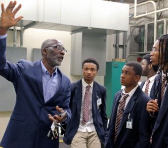 A man in a suit and tie is talking to a group of students.