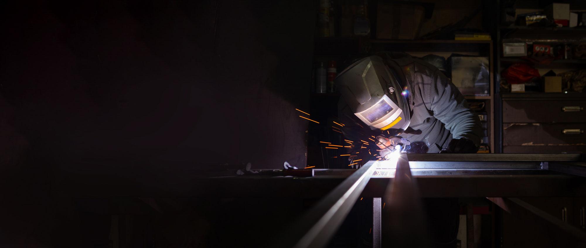 A welder working on a piece of metal in a dark room.