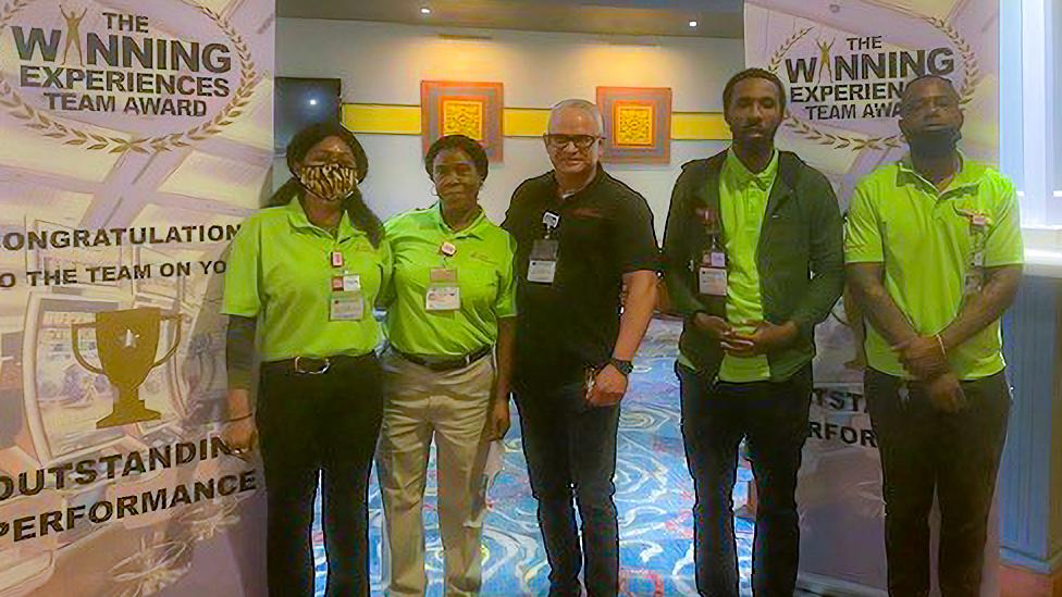 A group of people in green shirts standing in front of a banner.