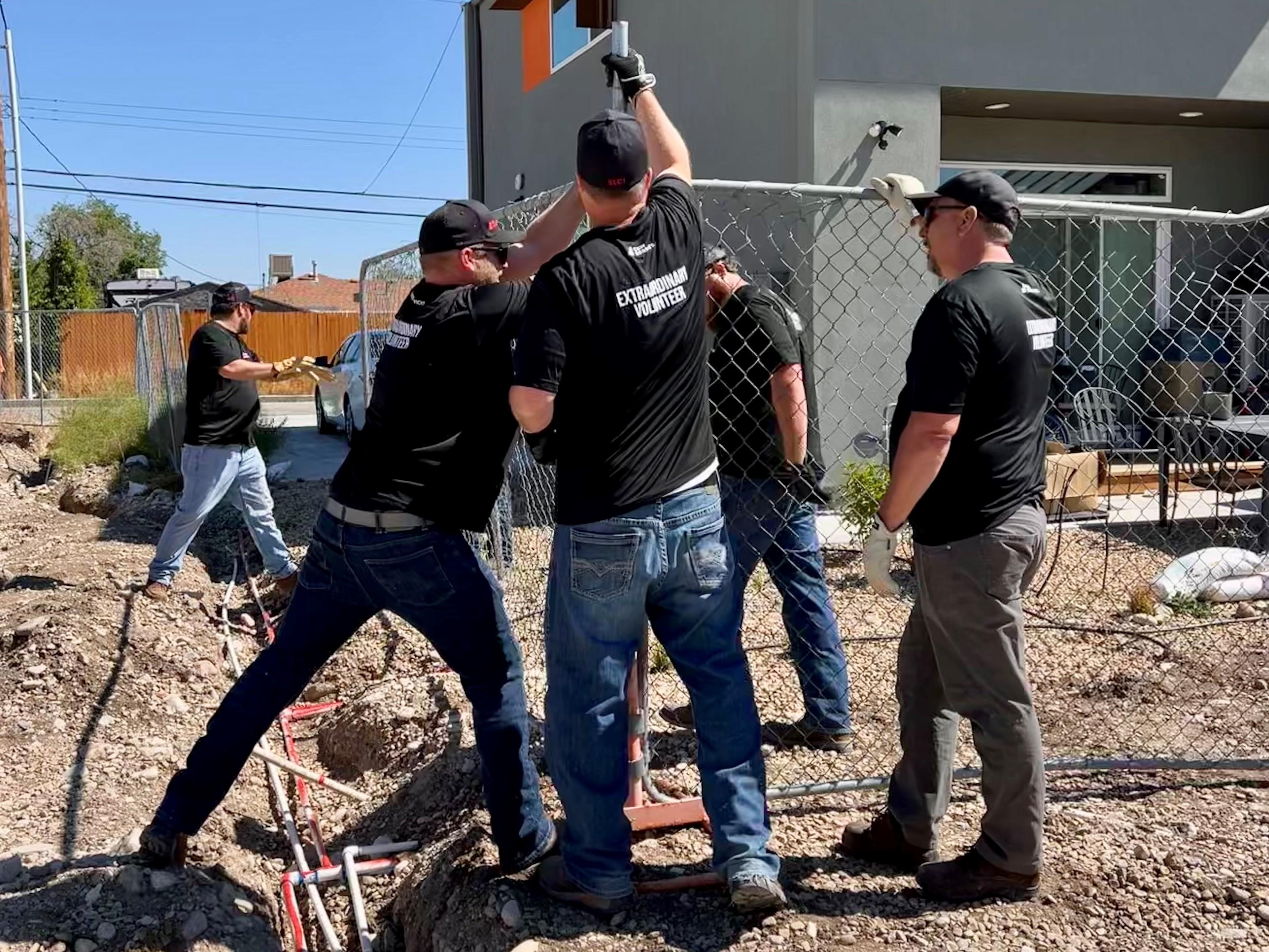 C&W Services employees wearing "Extraordinary Volunteers" tshirts installing a chain link fence fence post