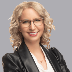 A smiling woman wearing glasses and a leather jacket.