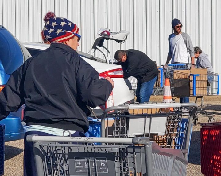 A group of people with shopping carts in a parking lot.