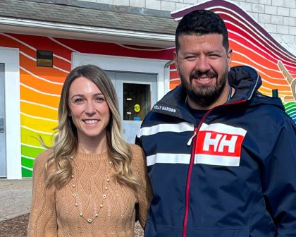 Woman and man standing in front of a mural painted on the side of a school building.