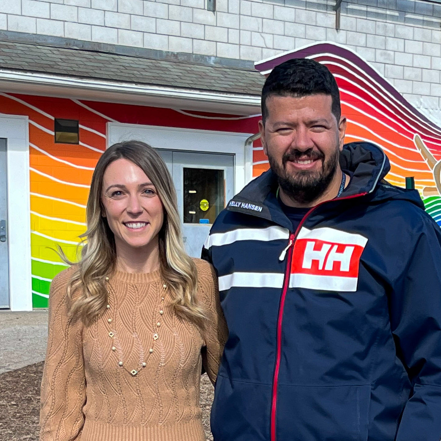 Woman and man standing in front of a mural painted on the side of a school building.