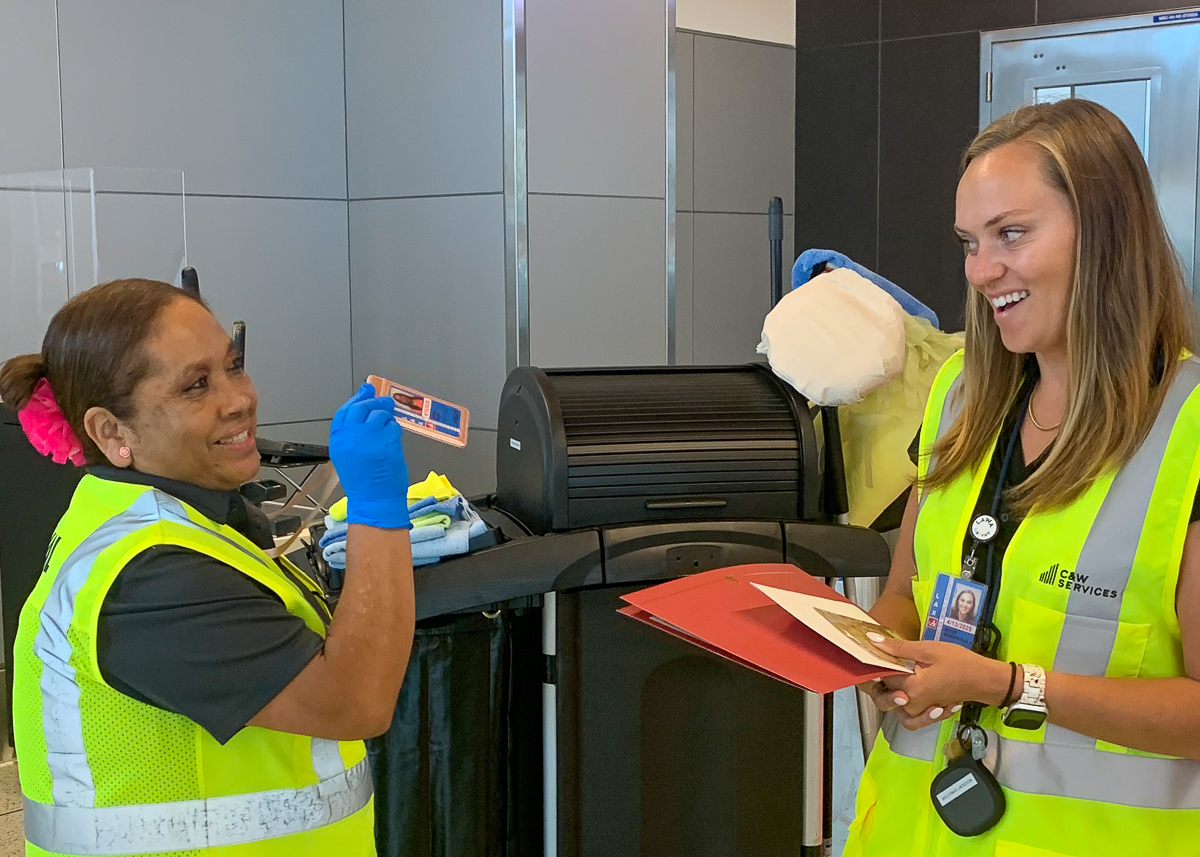 Two smiling women wearing safety vests. One woman gives another a certificate of appreciation and a gift card.