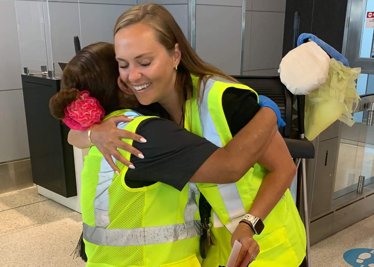 Two smiling women wearing safety vests hugging
