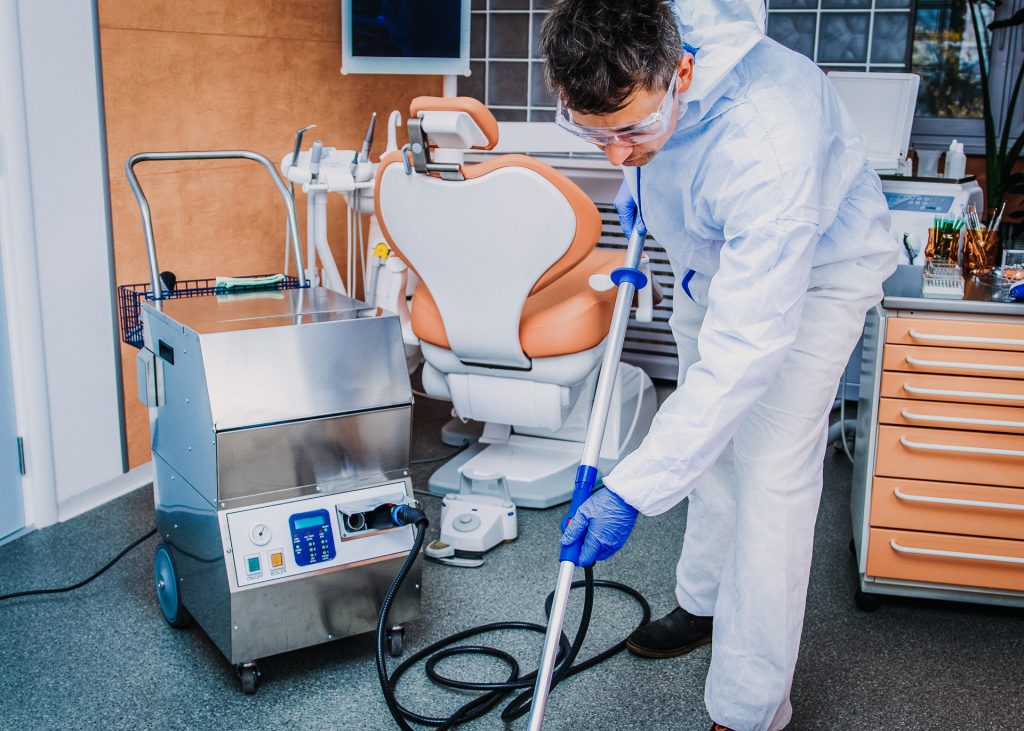 A man cleaning a dental chair with a vacuum.