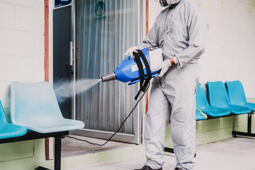 A person in a protective suit spraying plastic chairs in a waiting room