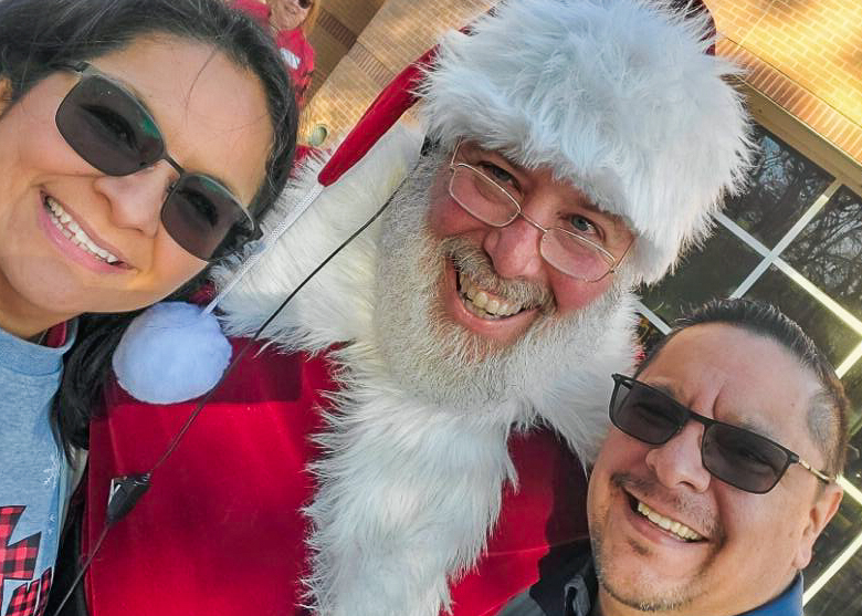 Three people posing for a photo with santa claus.