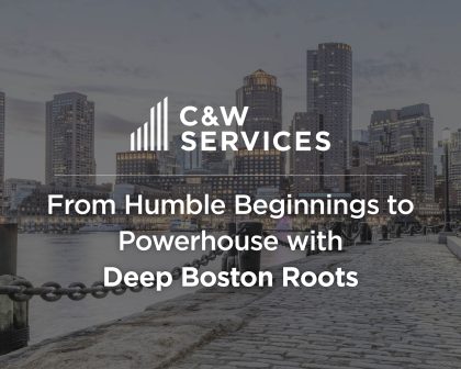C&W Services text overlay on an image of a Boston waterfront with cobblestones, buildings, and a chain railing. The text reads: 